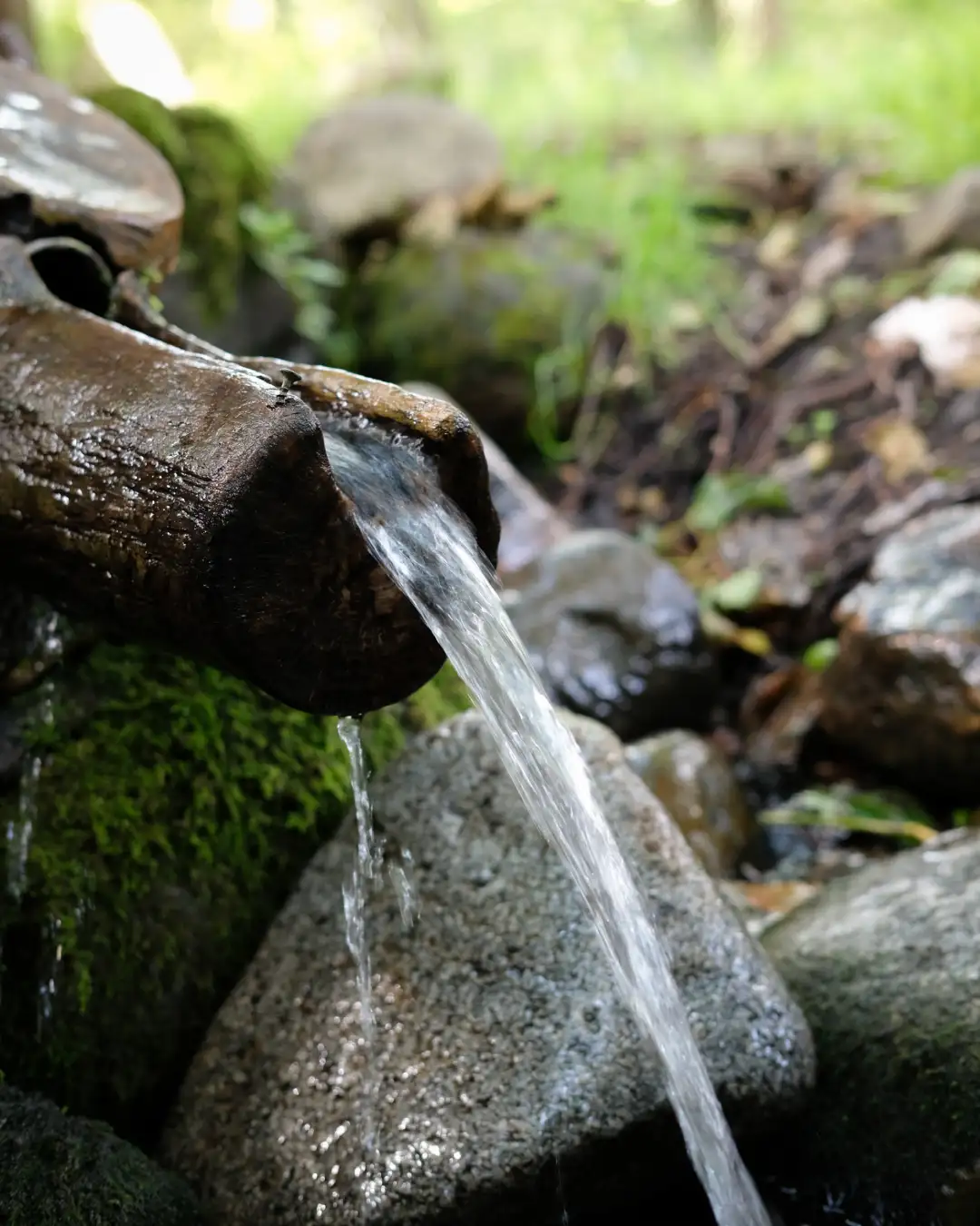 A stream of water flowing down from a wooden pipe. Created and photographed by Hiroku