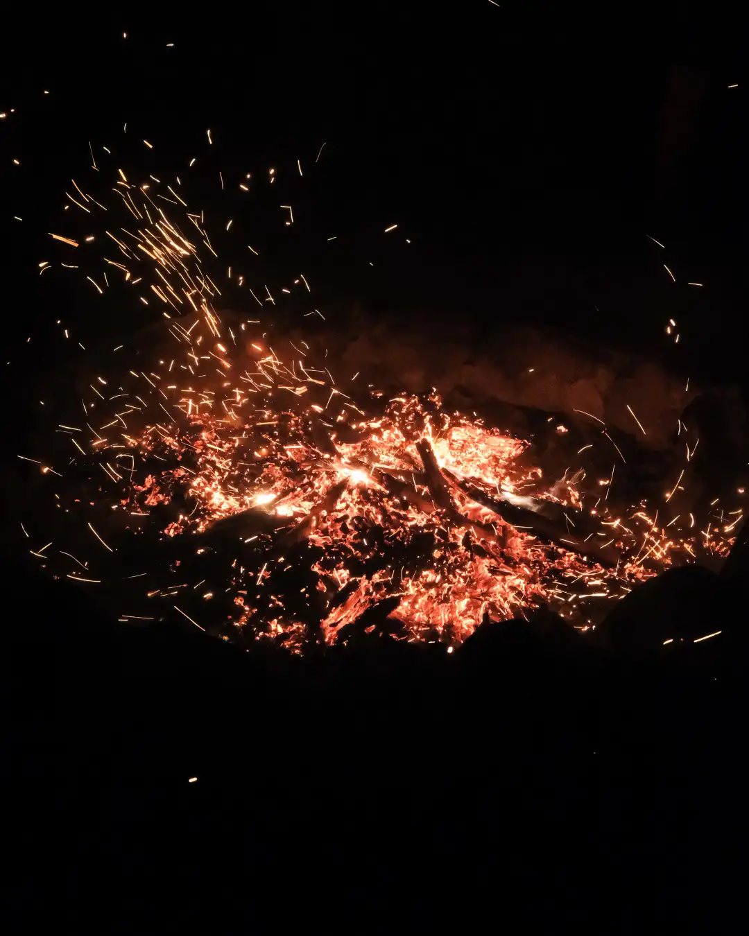 A hot campfire with a low of embers flowing in the wind at night. Created and photographed by Hiroku